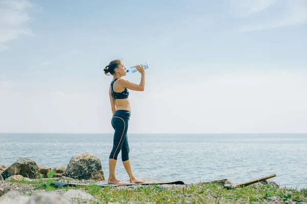 Menina atlética bebe água de uma garrafa na costa após um treino — Fotografia de Stock