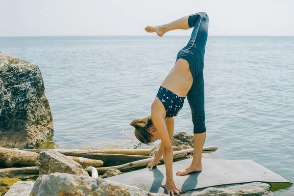 Jovem está envolvida em meditação, alongamento, ioga no fundo da praia — Fotografia de Stock