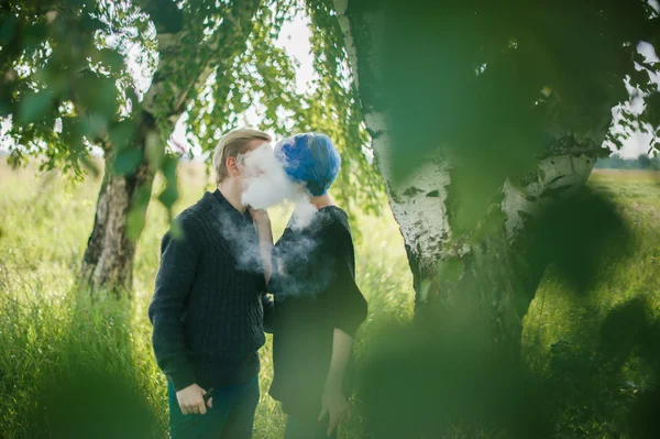 young couple with dyed hair smoking electronic cigarettes near birches. cloud head. cloud chasing