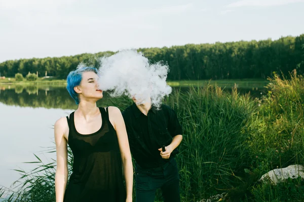 Giovane coppia con capelli tinti fumare sigarette elettroniche sul lago — Foto Stock