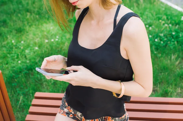 젊은 여자는 검은 티셔츠에 슬림 마당에 앉아 스마트폰을 사용 하 여 — 스톡 사진