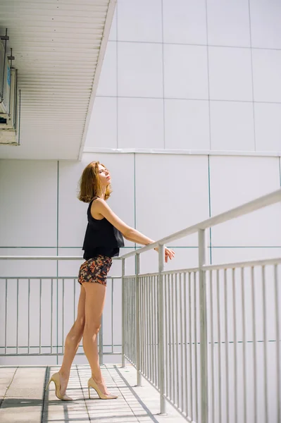 Beautiful slim girl in shorts and t-shirt standing on bolkone looking into the distance — Stock Photo, Image