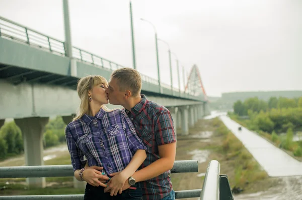 Hombre y mujer en la camisa a cuadros beso lindo abrazo de pie en las escaleras del puente — Foto de Stock