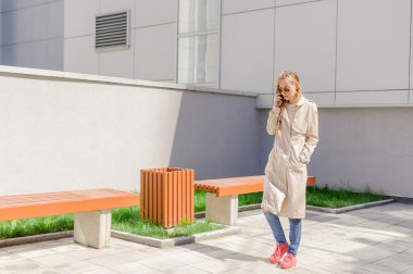 sokakta cep telefonuyla konuşurken bir yağmurluk giyen genç güzel kız Rüzgar, Fanlı uzun saçlı. Telefon bağlantı, irtibat, işiyle ilgili hoş sohbet