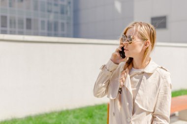 sokakta cep telefonuyla konuşurken bir yağmurluk giyen genç güzel kız Rüzgar, Fanlı uzun saçlı. Telefon bağlantı, irtibat, işiyle ilgili hoş sohbet