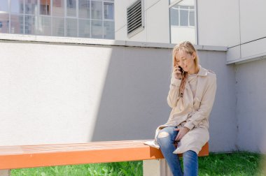 sokakta cep telefonuyla konuşurken bir yağmurluk giyen genç güzel kız Rüzgar, Fanlı uzun saçlı. Telefon bağlantı, irtibat, işiyle ilgili hoş sohbet