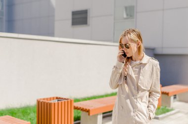 sokakta cep telefonuyla konuşurken bir yağmurluk giyen genç güzel kız Rüzgar, Fanlı uzun saçlı. Telefon bağlantı, irtibat, işiyle ilgili hoş sohbet