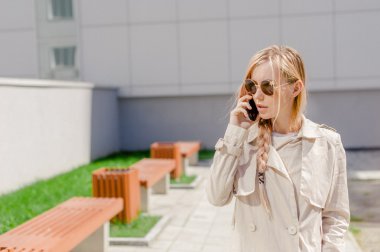 sokakta cep telefonuyla konuşurken bir yağmurluk giyen genç güzel kız Rüzgar, Fanlı uzun saçlı. Telefon bağlantı, irtibat, işiyle ilgili hoş sohbet