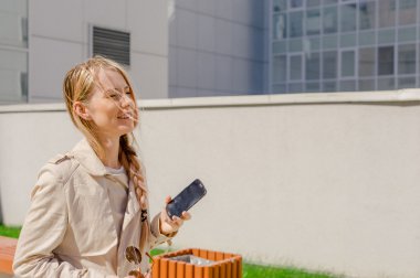 şık kız smartphone sokak, giymiş mavi kot pantolon ve beyaz bir T-shirt ve yağmurluk, bahçedeki boyalı uzun saçlı sms gönderir, aşırı tepki Interent sörf