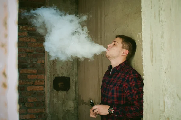 Hombre en una camisa a cuadros y jeans, fuma un cigarrillo electrónico —  Fotos de Stock