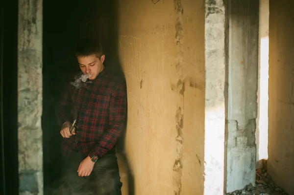 Homem de camisa xadrez e jeans, fuma um cigarro eletrônico — Fotografia de Stock
