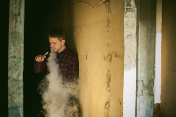 Hombre en una camisa a cuadros y jeans, fuma un cigarrillo electrónico — Foto de Stock