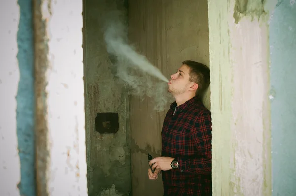 Homem de camisa xadrez e jeans, fuma um cigarro eletrônico — Fotografia de Stock