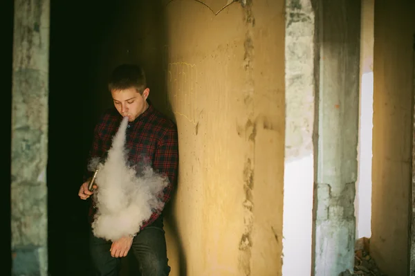 Man in a plaid shirt and jeans, smokes an electronic cigarette — Stock Photo, Image