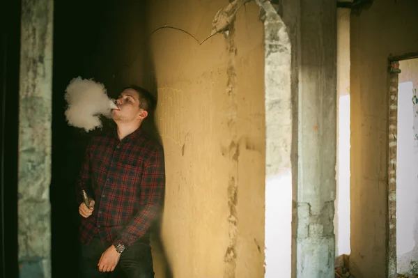 Hombre en una camisa a cuadros y jeans, fuma un cigarrillo electrónico — Foto de Stock