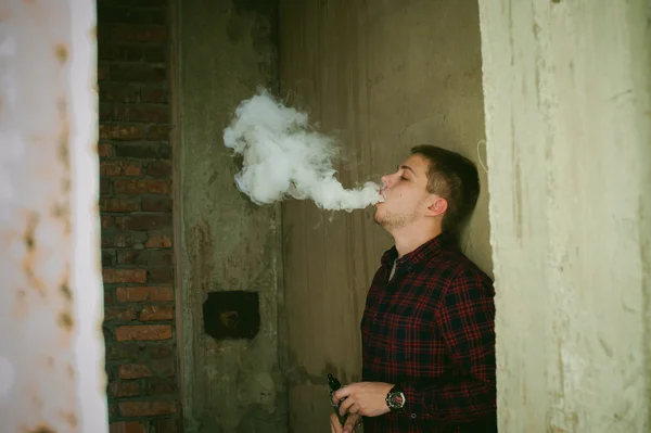 Uomo in camicia a quadri e jeans, fuma una sigaretta elettronica — Foto Stock