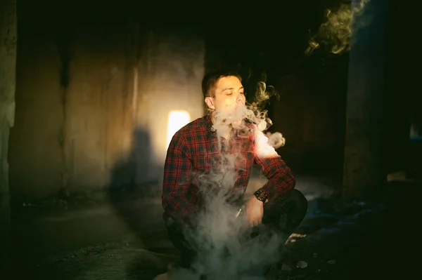 Adam bir ekose gömlek ve kot pantolon, elektronik sigara içiyor — Stok fotoğraf