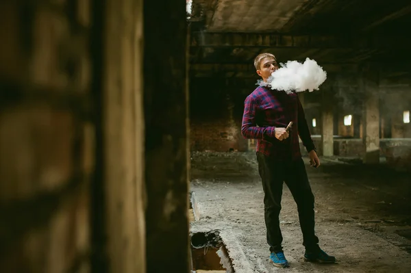 Homem de camisa xadrez e jeans, fuma um cigarro eletrônico — Fotografia de Stock