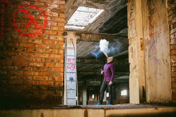 Hombre en una camisa a cuadros y jeans, fuma un cigarrillo electrónico — Foto de Stock