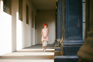 ile soluk pembe elbiseli kız Kızıl saçlı, beyaz bir sırt çantası elinde, ışık ve gölge sütunların güneşli yaz günü yürüyüş boyalı