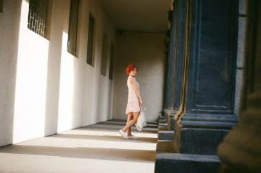 ile soluk pembe elbiseli kız Kızıl saçlı, beyaz bir sırt çantası elinde, ışık ve gölge sütunların güneşli yaz günü yürüyüş boyalı