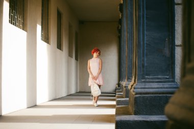 ile soluk pembe elbiseli kız Kızıl saçlı, beyaz bir sırt çantası elinde, ışık ve gölge sütunların güneşli yaz günü yürüyüş boyalı