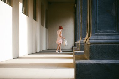 ile soluk pembe elbiseli kız Kızıl saçlı, beyaz bir sırt çantası elinde, ışık ve gölge sütunların güneşli yaz günü yürüyüş boyalı