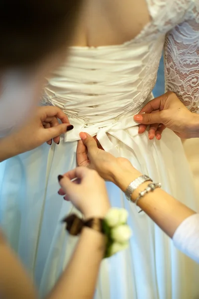 bridesmaid helps to tie a bow on a festive white dress of the bride on the wedding day. moment of life. wedding tradition, the bride\'s morning