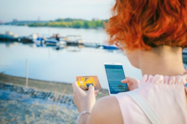 gün batımında, nehir kenarında yürüyüş kırmızı saçlı kız, aygıttan bir banka banka kartı kullanarak online alışveriş için ödeme yapmak için. Online ödeme, banka havaleleri.