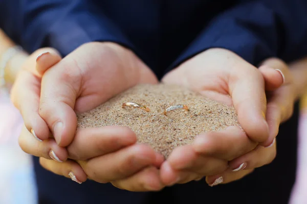 Пара держит кольца в руках на песке — стоковое фото