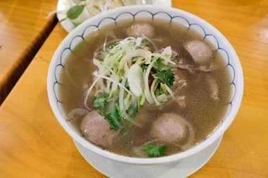 Vietnam bifteği ve sığır köftesi çorbası üzerine taze soğan ve otlar ve beyaz bir kasede servis edilen fotokopi alanı.