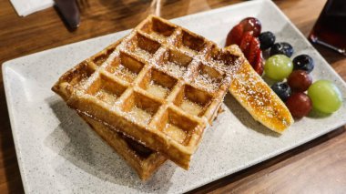 Üzerine pudra şekerli Belçika waffleları, ballı karamelize edilmiş muz dilimi ve üzümler, çilekler ve yabanmersini içeren küçük bir çeşit taze meyve karışımı.