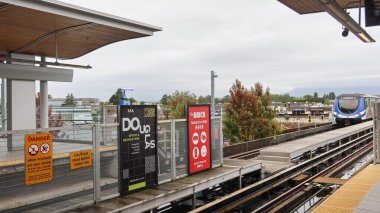 Lansdowne, Richmond, British Columbia, Kanada - 3 Ekim 2025: bölünme çitlerinde reklam panosu reklamlarıyla perona yaklaşan metro treni