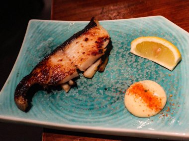 Izgara Japon Miso Black Cod ya da ızgara Miso-Marinated Sablefish, yanında limon dilimi ve mayonez sosu ile birlikte, yemyeşil, mavi, fotokopi alanı olan bir tabak.
