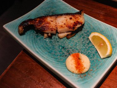 Izgara Japon Miso Black Cod ya da ızgara Miso-Marinated Sablefish, yanında limon dilimi ve mayonez sosu ile birlikte, yemyeşil, mavi, fotokopi alanı olan bir tabak.