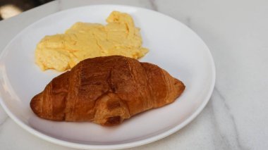 Çırpılmış yumurta ve kruvasanı fotokopi alanı olan beyaz bir tabakta kapat.