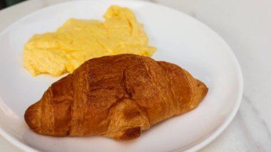 Çırpılmış yumurta ve kruvasanı fotokopi alanı olan beyaz bir tabakta kapat.