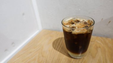 Buzlu kahvenin yanına limon suyu koy ve beyaz duvarlı, ahşap masanın sağ alt köşesine koy.