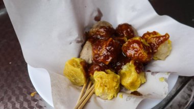 Hong Kong tarzı Çin sokak yemekleri Shu mai ve sığır eti topu da dahil olmak üzere tabağa yerleştirilmiş bir kağıt üzerine baharatlı tatlı sos eklendi.