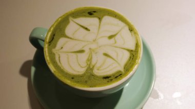 Yeşil çaylı latte (matcha latte) ve yeşil mavi bir fincanın üzerinde fotokopi alanı olan kahve sanatı.