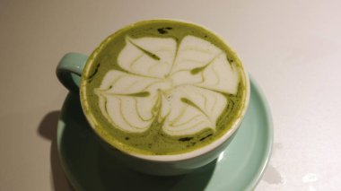 Yeşil çaylı latte (matcha latte) ve yeşil mavi bir fincanın üzerinde fotokopi alanı olan kahve sanatı.