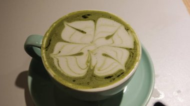 Yeşil çaylı latte (matcha latte) ve yeşil mavi bir fincanın üzerinde fotokopi alanı olan kahve sanatı.