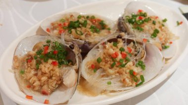 Hong Kong usulü dört parça haşlanmış midye sarımsak, yeşil soğan, kırmızı biber ve kırmızı biberli makarna ile servis edilir.