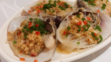 Hong Kong usulü dört parça haşlanmış midye sarımsak, yeşil soğan, kırmızı biber ve kırmızı biberli makarna ile servis edilir.