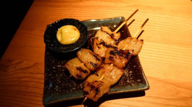 İki ızgara Japon Pork Jowl (domuz boynu eti) şiş mayonez sosu ile siyah bir tabakta, kopyalama alanı var
