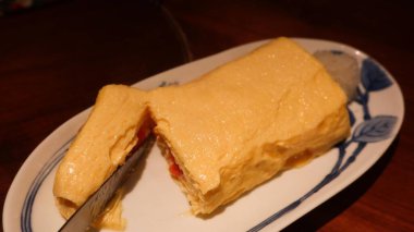 Japon rulo omletini yakın çekim bıçakla dilimlenerek içindeki mentaiko dolgusu izakya restoranında fotokopi alanı olan geleneksel bir tabakta servis ediliyor.