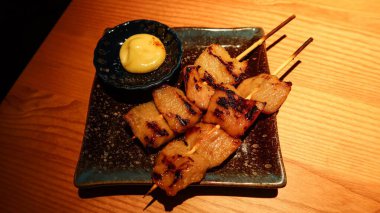 İki ızgara Japon Pork Jowl (domuz boynu eti) şiş mayonez sosu ile siyah bir tabakta, kopyalama alanı var