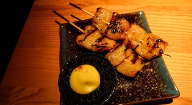 İki ızgara Japon Pork Jowl (domuz boynu eti) şiş mayonez sosu ile siyah bir tabakta, kopyalama alanı var