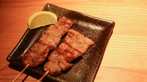 Japon sığır eti dili şiş kapalı üzerinde siyah biber ve yanında limon dilimi ile fotokopi alanı ile siyah bir tabakta