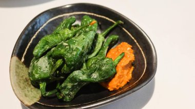 İspanyol İspanyol tapas Padrn biberinin yanına baharatlı acı biber sosu koyun ve siyah tabakta yer açın.